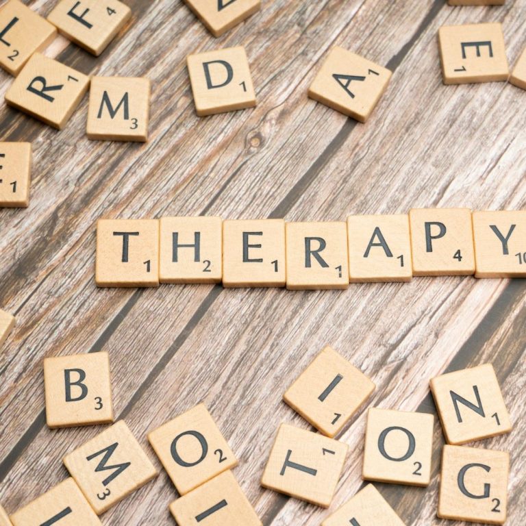 Holztablett mit Scrabble-Steinen, die das Wort "THERAPY" bilden.